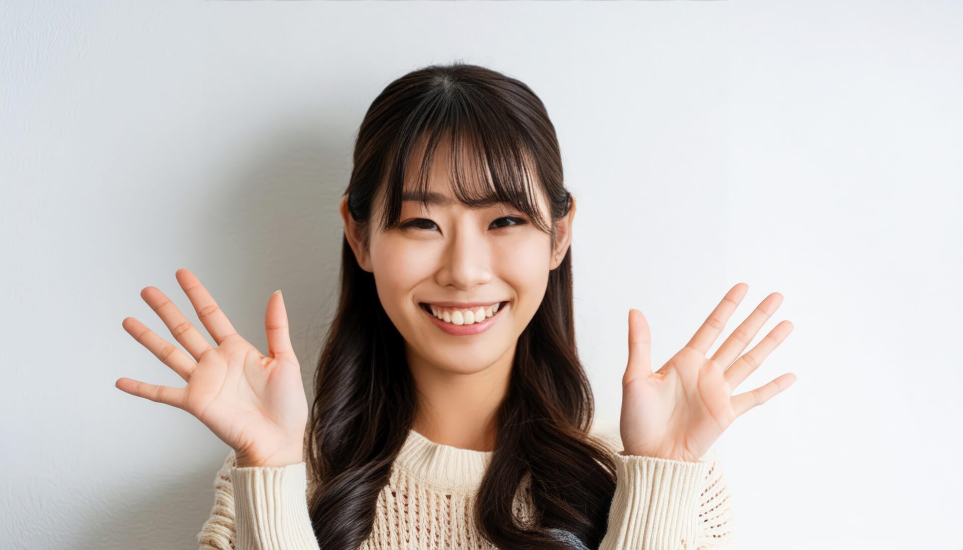 白背景で両手を広げるベージュニットを着た若い女性