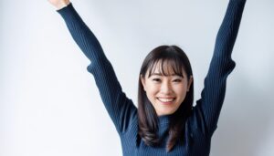 白背景で両腕を上げるリブニット姿の若い女性