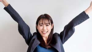白背景で両腕を上げるジャケット姿の若い女性