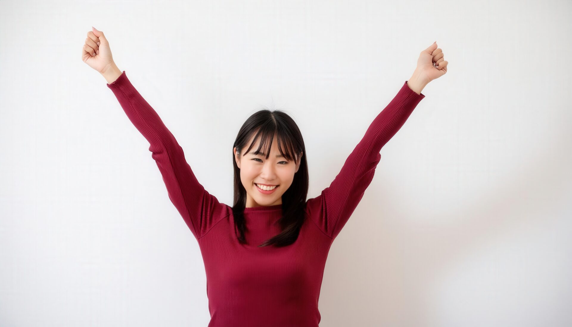 白背景で両腕を上げるワインレッドのトップスを着た若い女性