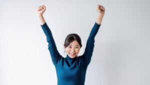 白背景で腕を高く上げる笑顔の若い女性（タートルネック）