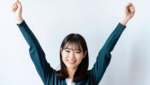 白背景で両腕を上げる笑顔の若い女性（前髪あり）