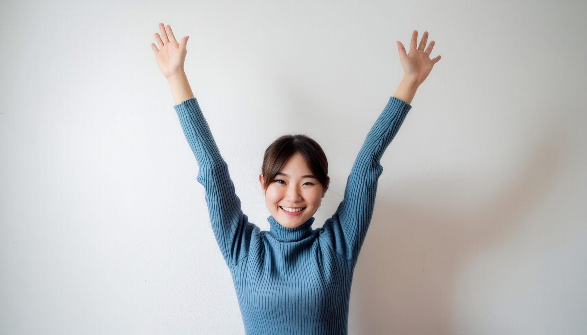 白背景で万歳をする笑顔の若い女性（ブルーのセーター）