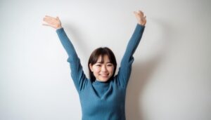 白背景で両手を挙げる笑顔の若い女性（ブルーのタートルネック）