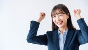 白背景でガッツポーズをする笑顔の若い女性（スーツ姿）