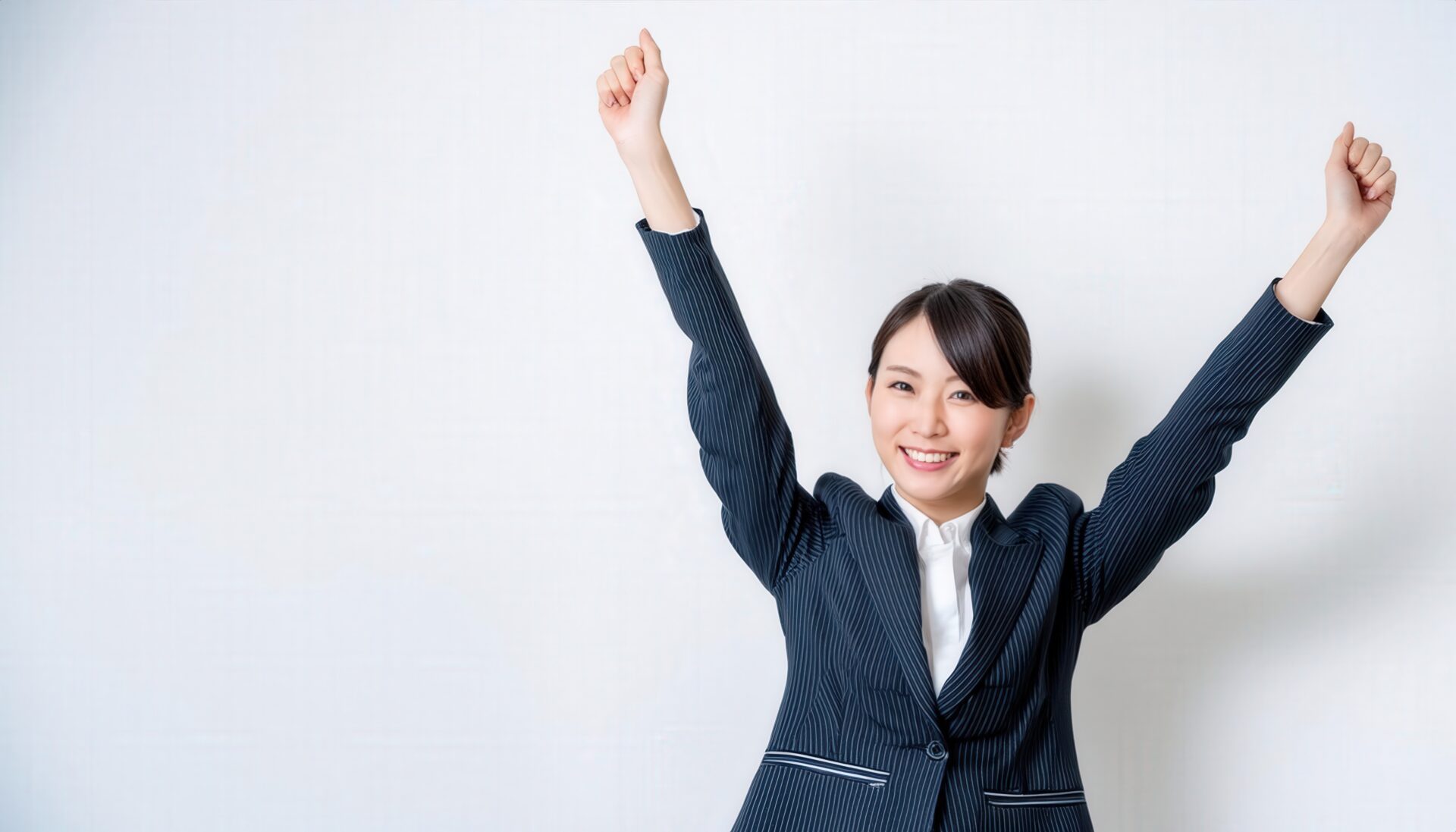 白背景で拳を上げる笑顔の若い女性（ストライプのスーツ）