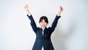 白背景で腕を高く上げる笑顔の若い女性（ストライプのスーツ）