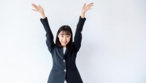 白背景で両腕を上げる笑顔の若い女性（ブラックスーツ・前髪あり）