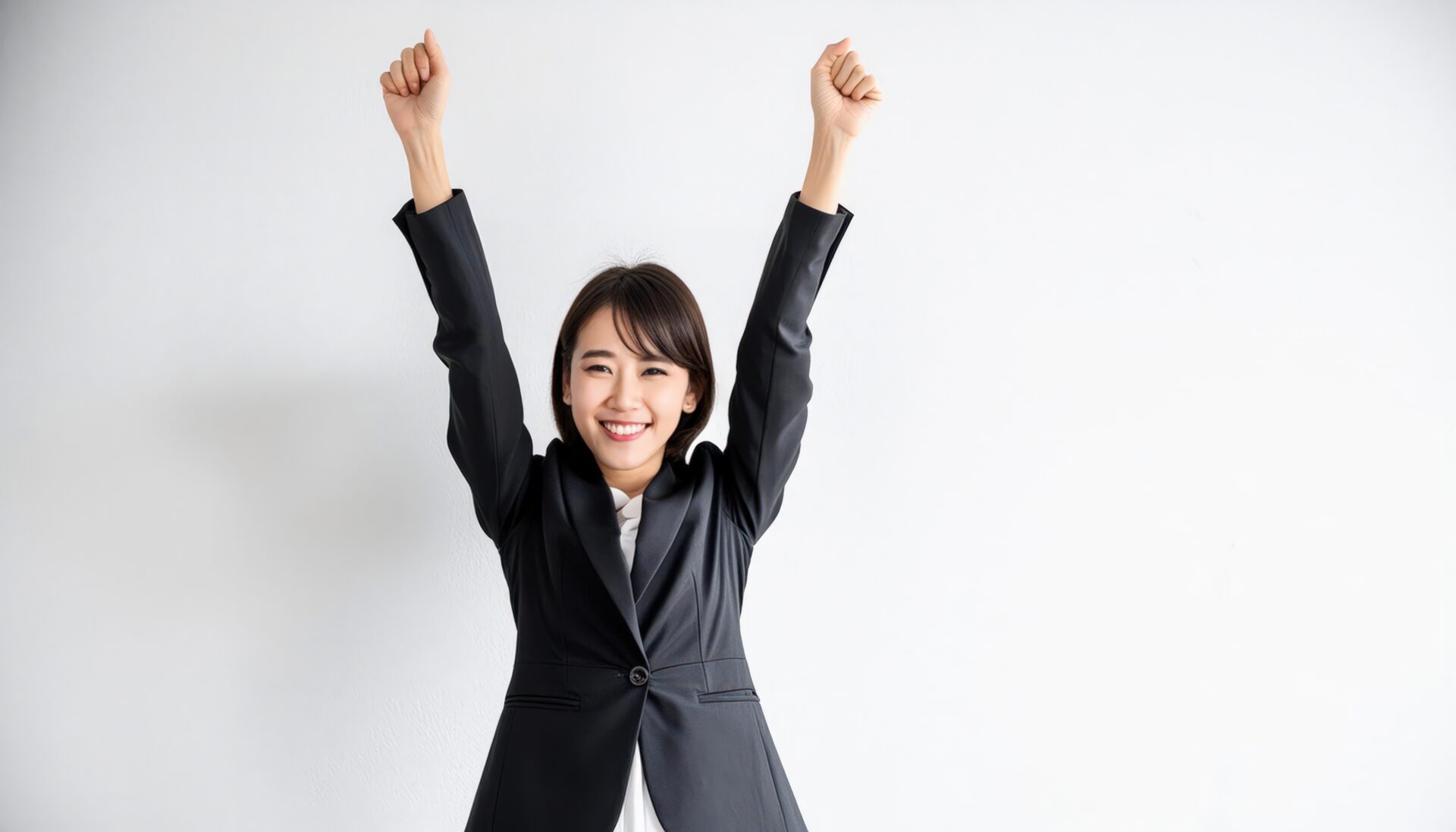 白背景で拳を上げる笑顔の若い女性（ブラックスーツ）