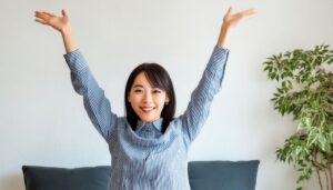 室内で両腕を上げる笑顔の若い女性（ストライプシャツ）