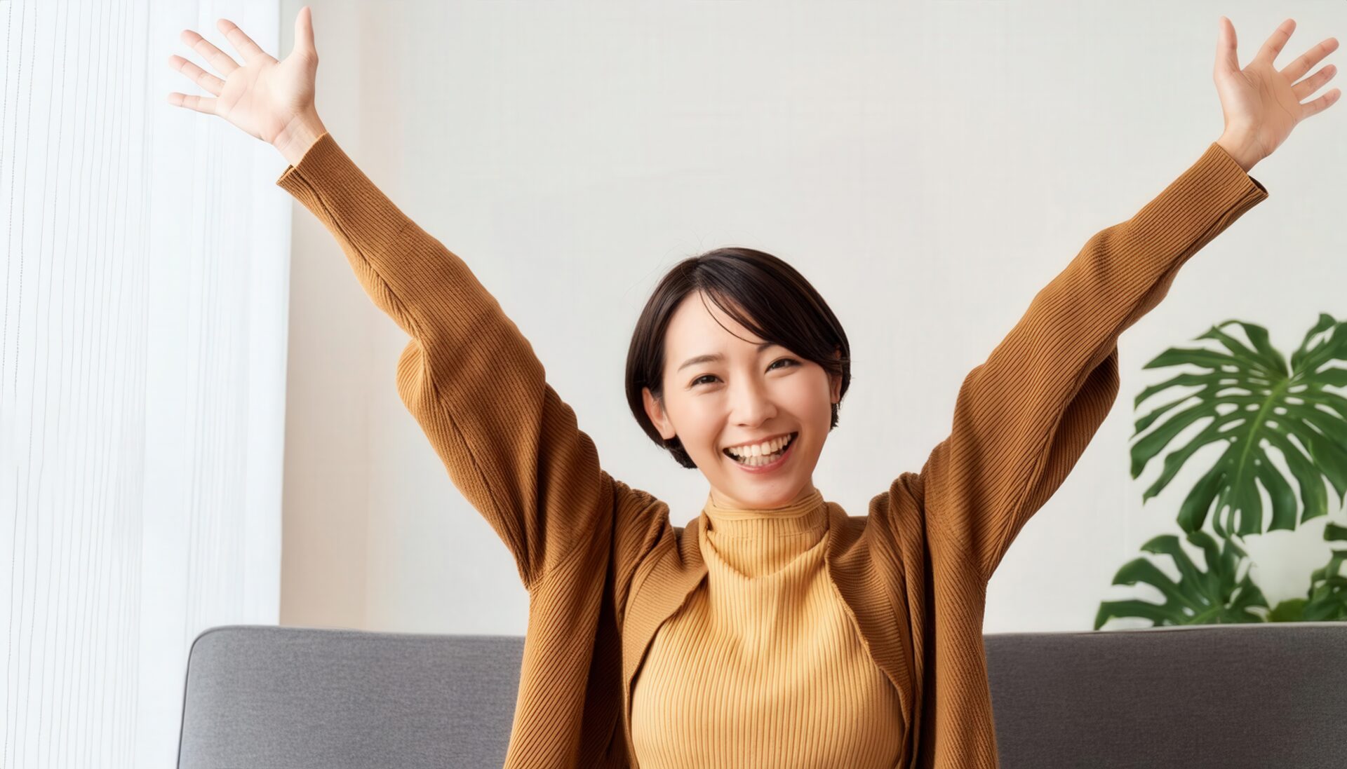 室内で万歳する笑顔の若い女性（ブラウンのトップス）