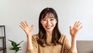 室内で手を挙げる笑顔の若い女性（ベージュのトップス）
