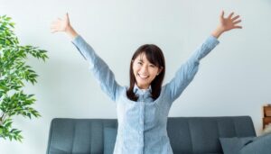 室内で両腕を広げる笑顔の若い女性（ストライプシャツ）