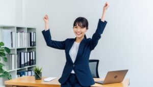 オフィスでガッツポーズをする若い女性（ネイビーのスーツ）