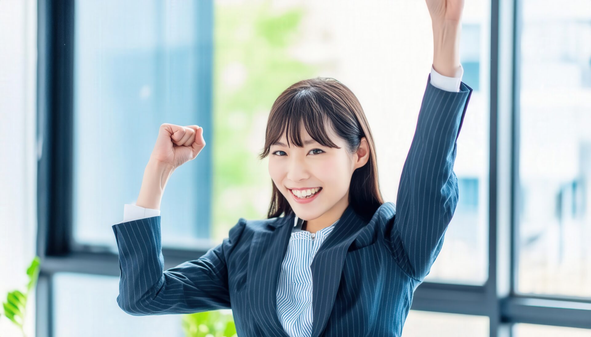 オフィスで拳を上げる若い女性（ストライプのスーツ）