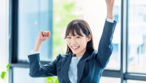 オフィスで拳を上げる若い女性（ストライプのスーツ）