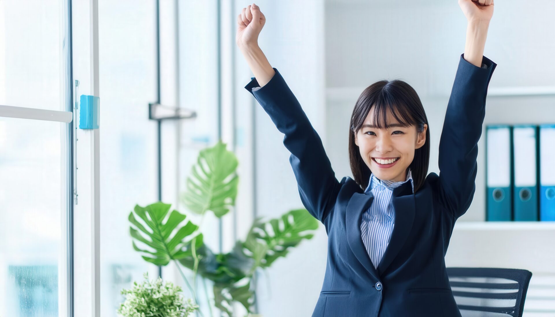 オフィスでガッツポーズをする若い女性（観葉植物のある室内）