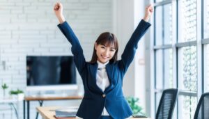 オフィスで両腕を上げる若い女性（窓際の室内）