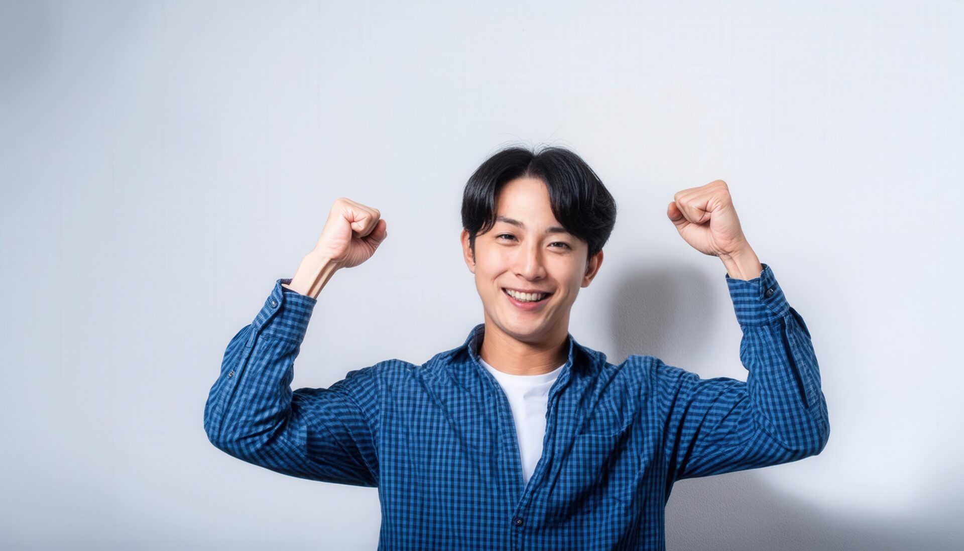 白背景でガッツポーズをする笑顔の若い男性（チェックシャツ）