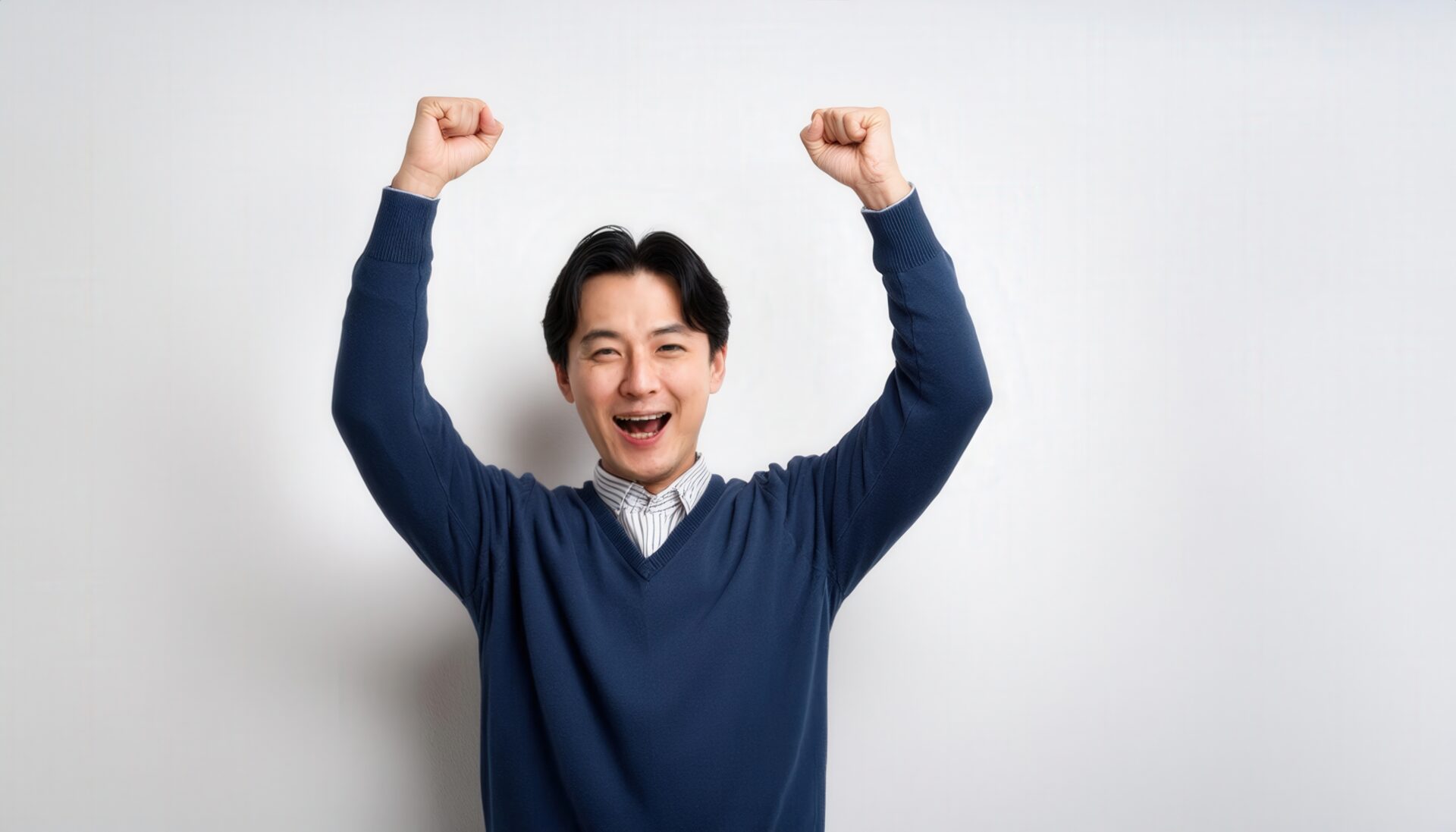 白背景でガッツポーズをする笑顔の若い男性（ネイビーのトップス）