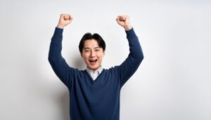 白背景でガッツポーズをする笑顔の若い男性（ネイビーのトップス）