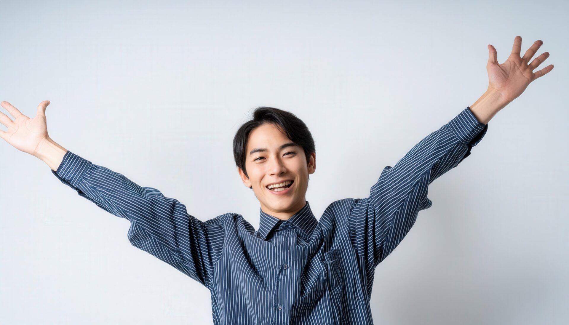 白背景で両腕を広げる笑顔の若い男性（ストライプシャツ）