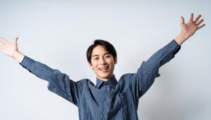 白背景で両腕を広げる笑顔の若い男性（ストライプシャツ）