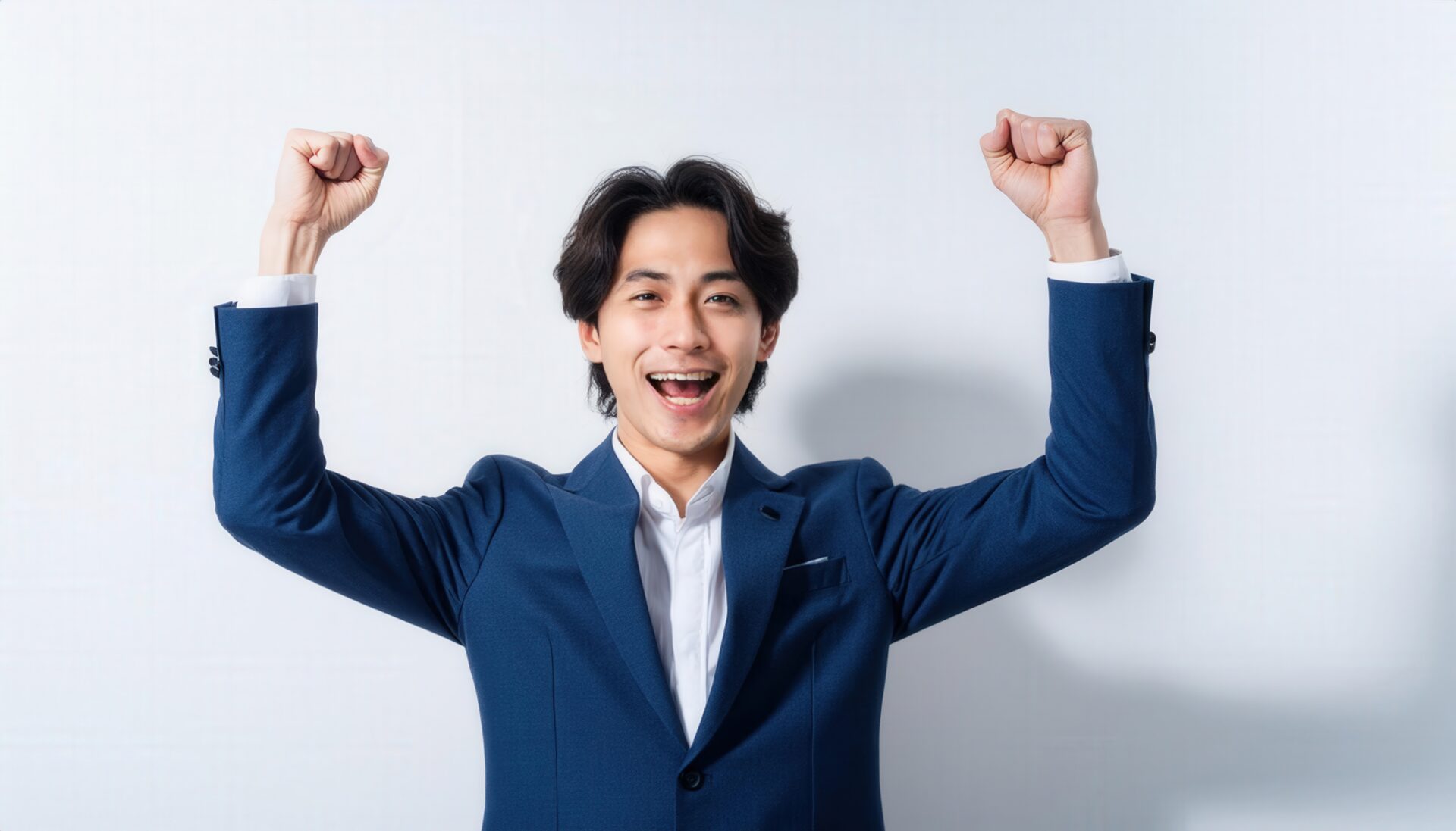 白背景で拳を上げる笑顔の若い男性（ネイビースーツ）