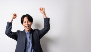 白背景でガッツポーズをする笑顔の若い男性（グレージャケット）