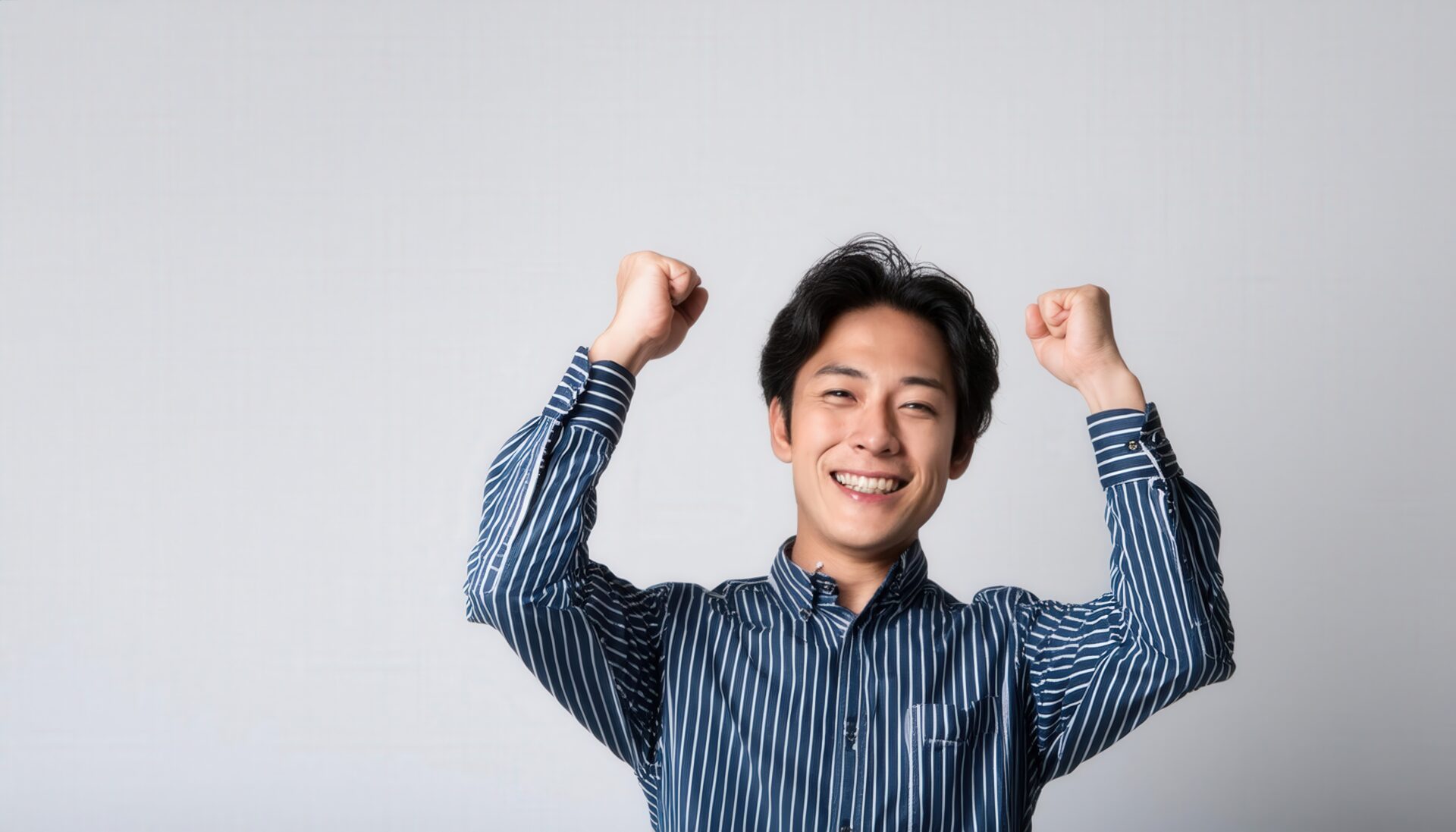 白背景でガッツポーズをする笑顔の若い男性（ストライプシャツ）