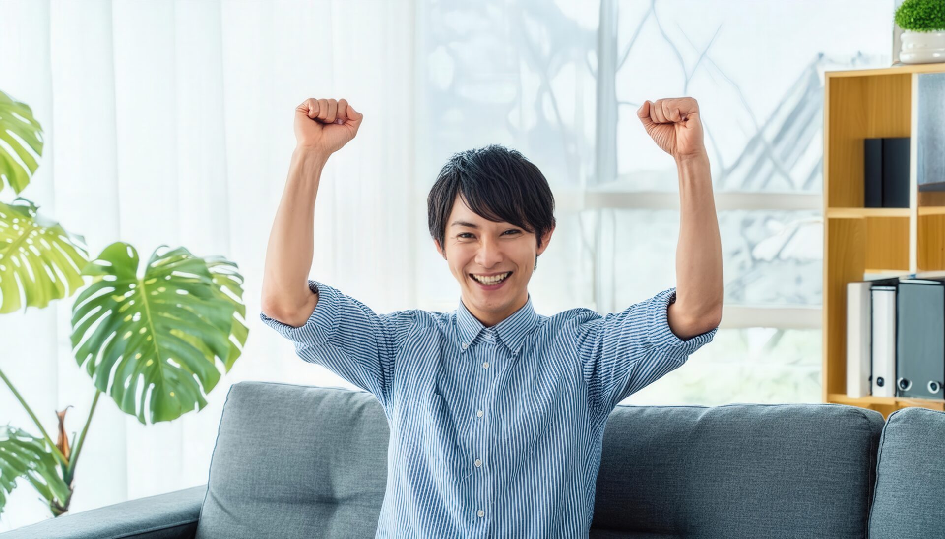 室内でガッツポーズをする若い男性（ストライプシャツ）