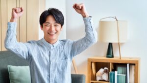 室内でガッツポーズをする若い男性（ストライプシャツ・木製家具）