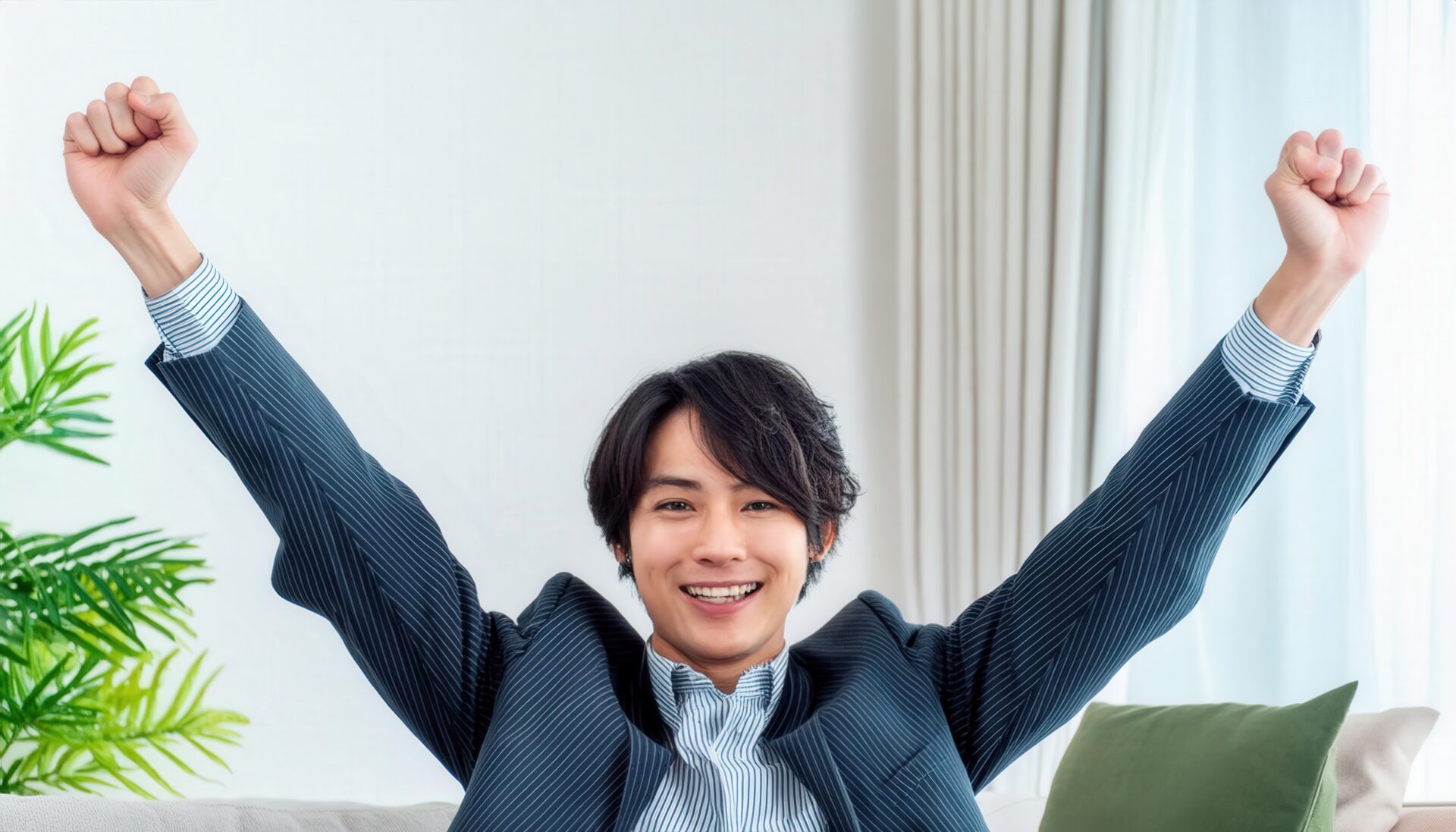 室内でガッツポーズをする若い男性（ストライプスーツ）