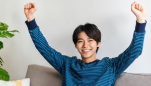 室内でガッツポーズをする若い男性（ボーダートップス）