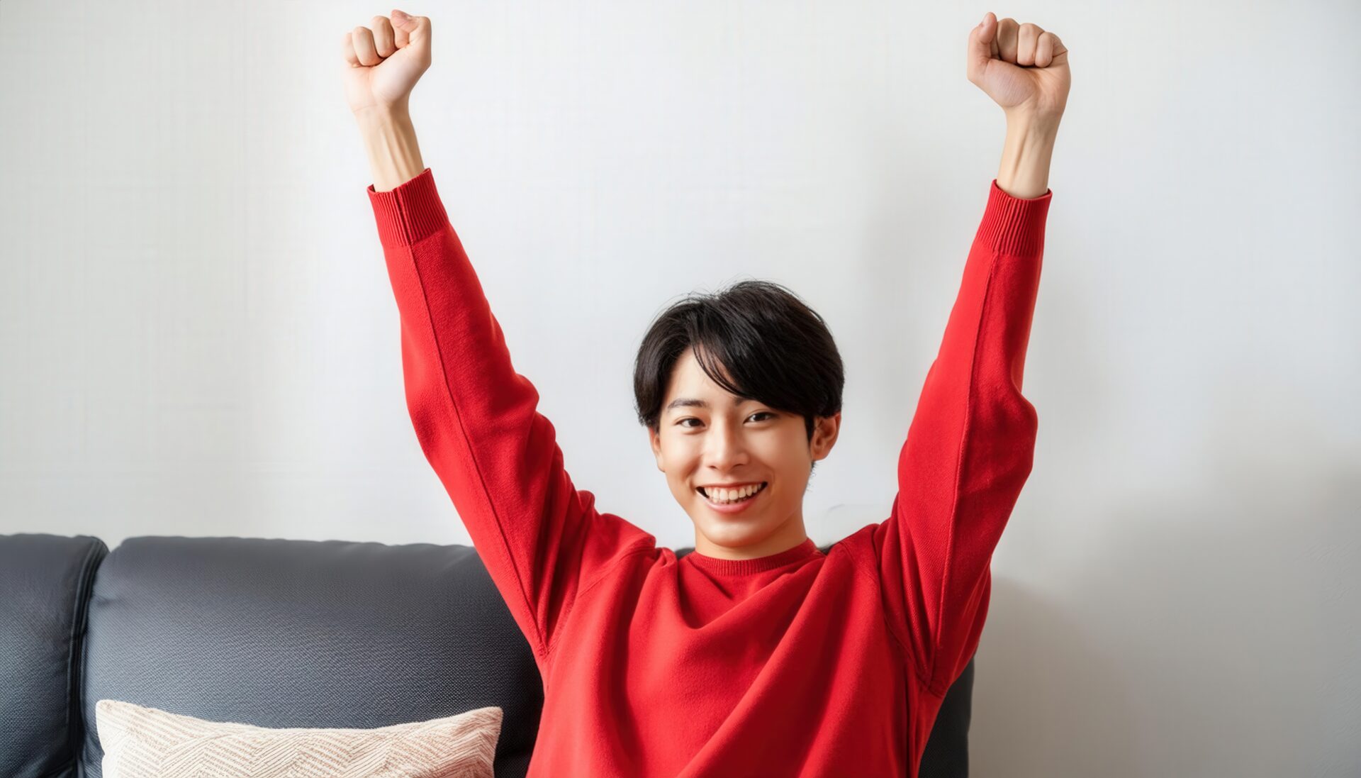 室内でガッツポーズをする若い男性（レッドトップス）