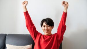 室内でガッツポーズをする若い男性（レッドトップス）