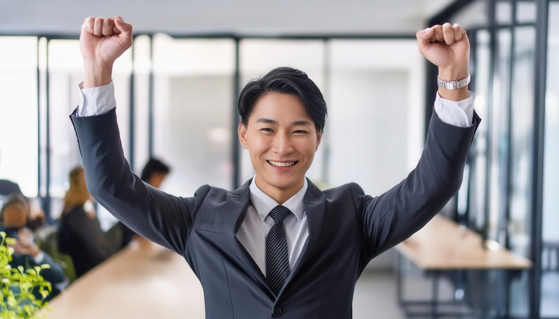 オフィスでガッツポーズをする若い男性（グレースーツ）