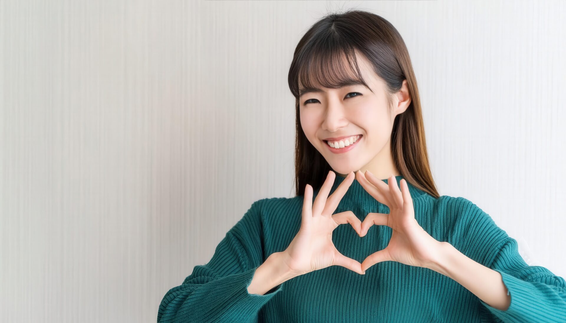 ハートマークを作る笑顔の若い女性（グリーントップス・前髪あり）