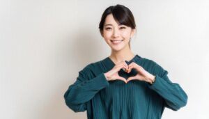 ハートマークを作る若い女性（グリーントップス・アップヘア）