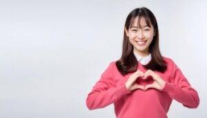 ハートマークを作る若い女性（ピンクトップス・白背景）