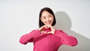 ハートマークを作る若い女性（ピンクトップス・ショートヘア）