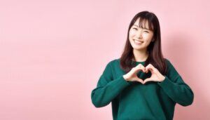 ピンク背景でハートマークを作る若い女性（グリーントップス）