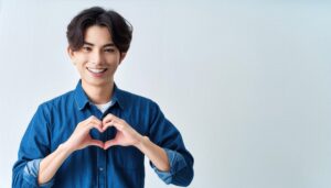 白背景でハートマークを作る若い男性（デニムシャツ）