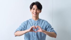 白背景でハートマークを作る若い男性（ストライプシャツ）