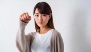 白背景で拳を突き出す若い女性（カーディガン）