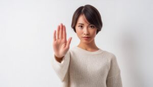 白背景でストップのポーズをする若い女性（ホワイトニット）