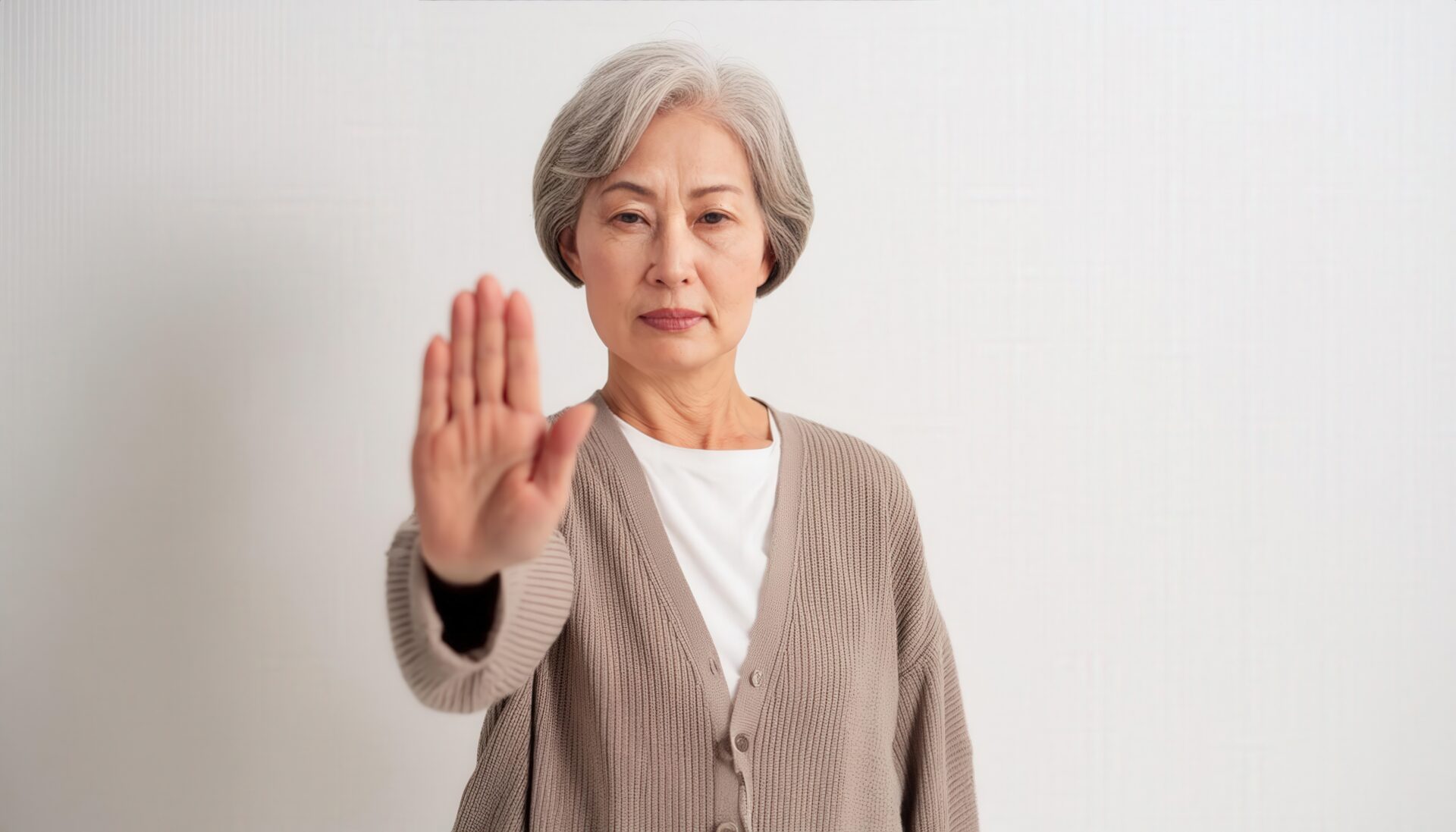 白背景で拒否の姿勢を見せるシニア女性