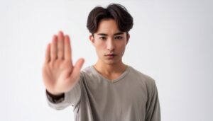 白背景で手のひらを前に突き出す若い男性（グレーTシャツ）