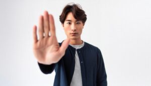 白背景でストップのジェスチャーをする若い男性（ネイビーシャツ）