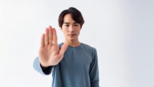 白背景で制止のポーズをとる若い男性（ブルーTシャツ）